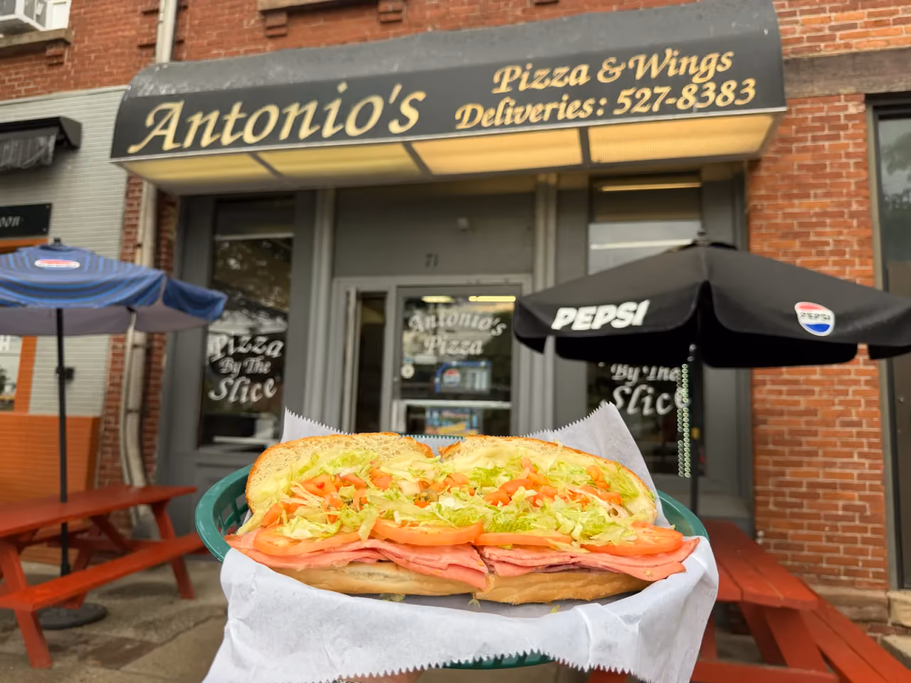 A 12-inch Italian sub held in front of the Antonio's Easthampton storefront